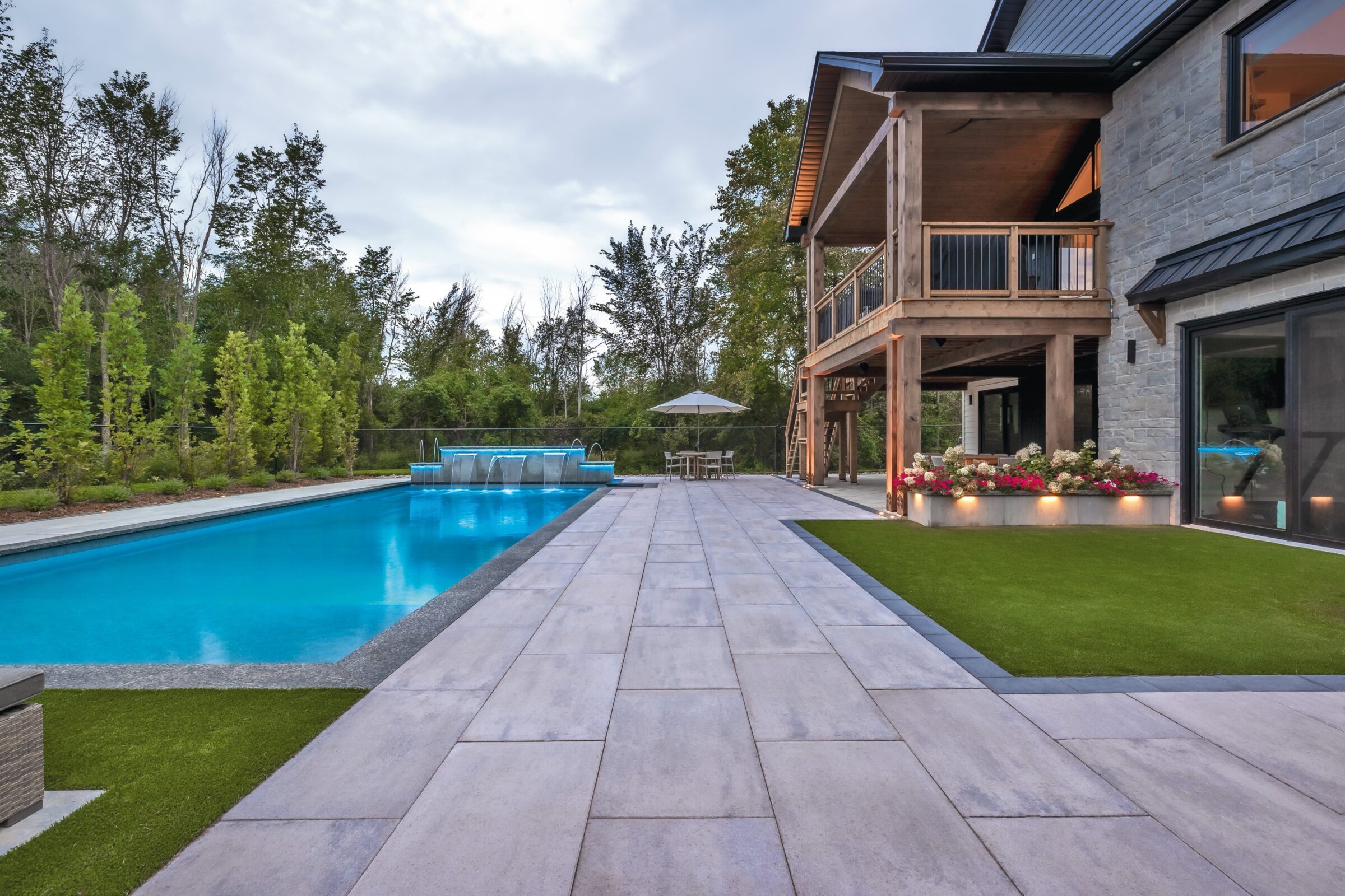 Modern house with a pool, surrounded by trees and landscaped garden, featuring a spacious patio and upper deck. No recognizable landmarks present.