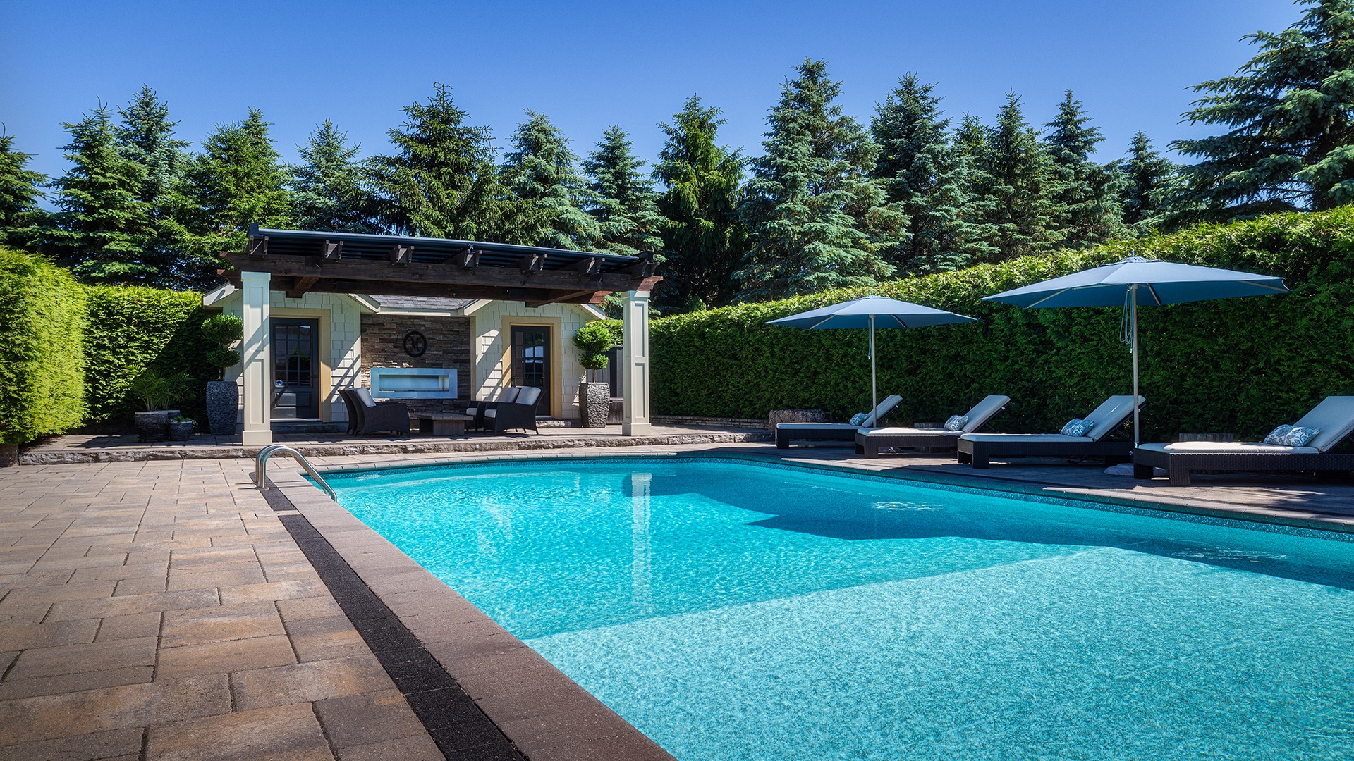 A serene backyard with a swimming pool, lounge chairs, umbrellas, and a cozy pergola, surrounded by lush greenery and tall trees.
