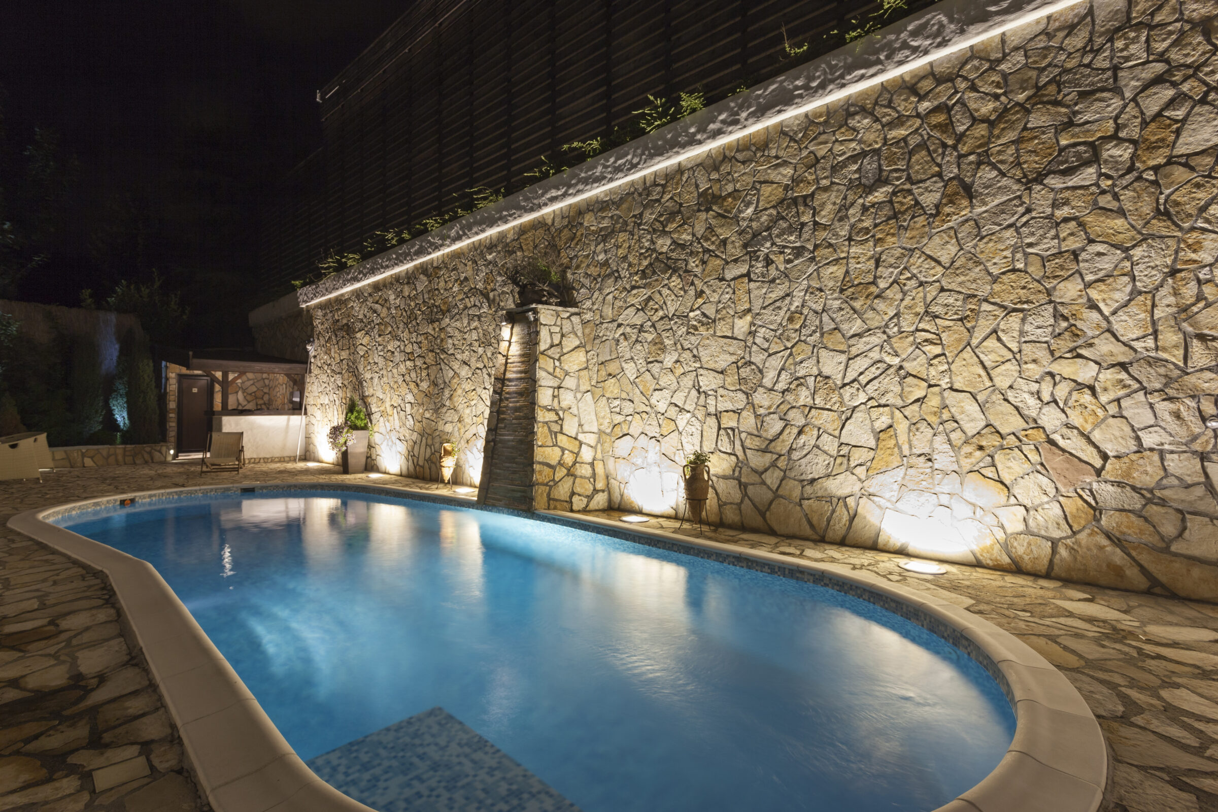 A pool surrounded by a stone wall is lit at night, creating a serene and inviting ambiance. No people or landmarks are visible.
